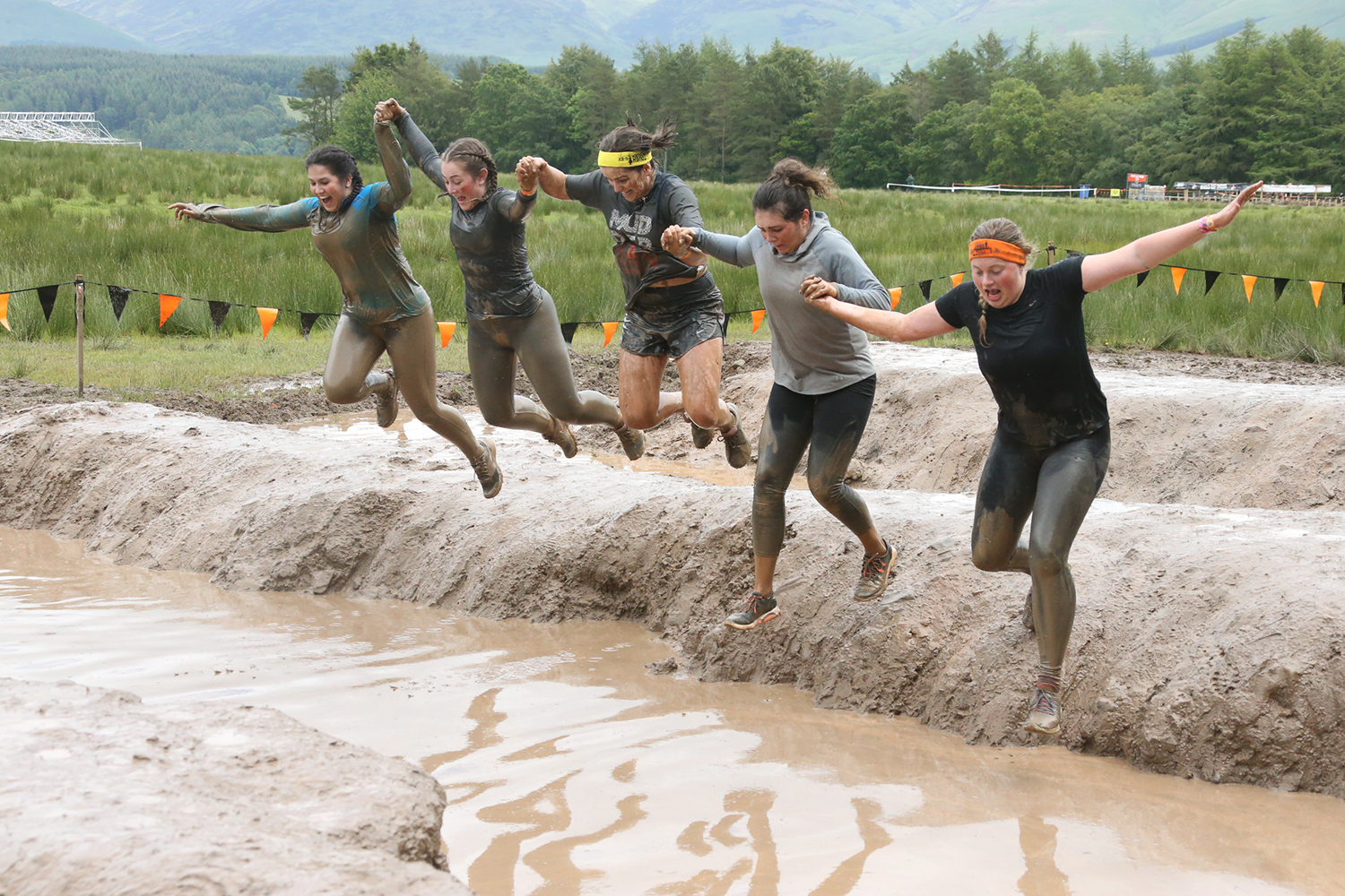 Team jumping "Mud Mile" at Tough Mudder event in Scotland.